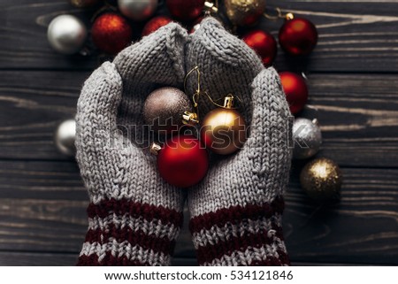 hands in gloves holding red and golden christmas balls and ornaments on rustic wooden background. space for text. top view. seasonal greetings concept. winter holidays decorations