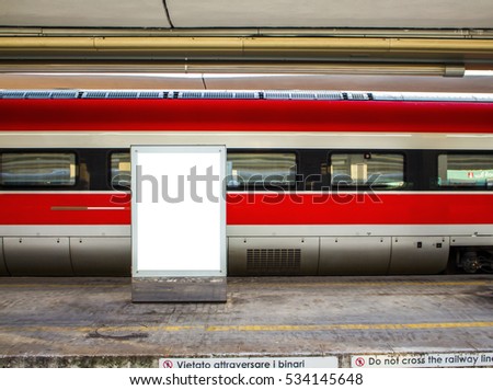 red train carriage behind a blank billboard, with empty platform