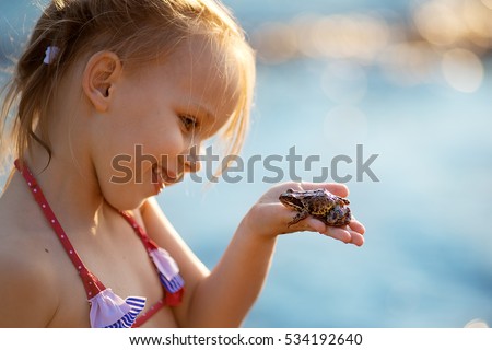 Pretty little girl with pigtails in swimsuit holding a frog. Nature and children.
