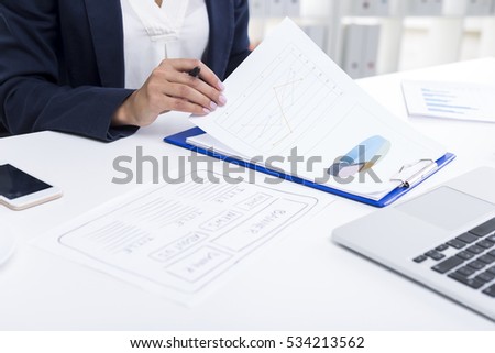 Close up of a tanned woman's hands. She is reading a document with a diagram and sitting at her workplace. Concept of computer design