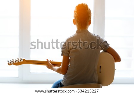 Silhouette of a beautiful young girl with a guitar near the window.