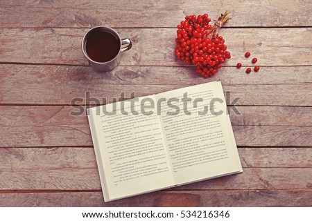 Cup of tea with open book and bunch of red rowan on wooden background