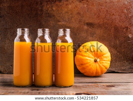 The fresh juice of ripe pumpkin bottled in small glass bottles. Dark wooden background