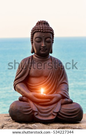 Buddha with a candle in hands and sea background. Vertical image. Royalty-Free Stock Photo #534227344