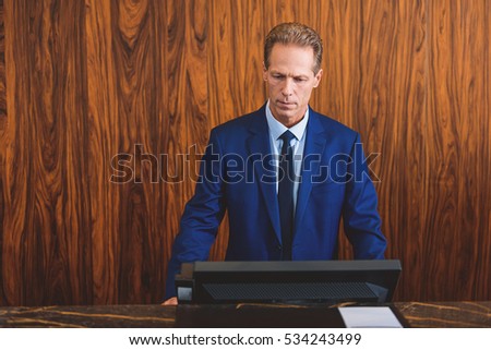 Mature hotelier standing at reception Royalty-Free Stock Photo #534243499