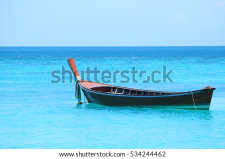 A wooden rowboat tied with colorful fabrics lied at anchor in the clear sea at Lipe island, Thailand in sunny day. Tourist boat in Andaman. Using as seascape, vacation, tourism, or natural background