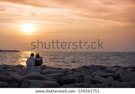 young couple sit on the beach  rock watching sunset 