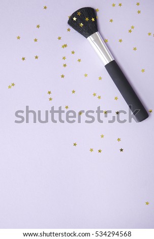 A large powder make up brush on a pastel purple background with gold glitter stars with blank space below