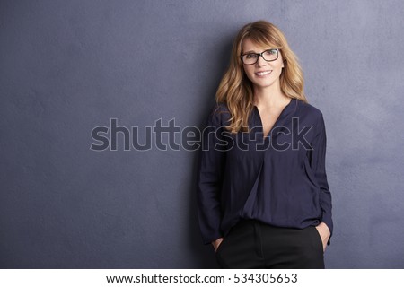 Portrait of a happy woman posing against a grey background while lying against the wall. 