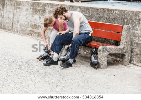 Young people friends in training suit putting on roller skates outdoor. Woman and man sitting on bench.