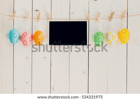 Easter egg and blank photo frame hanging on with white wood with space.