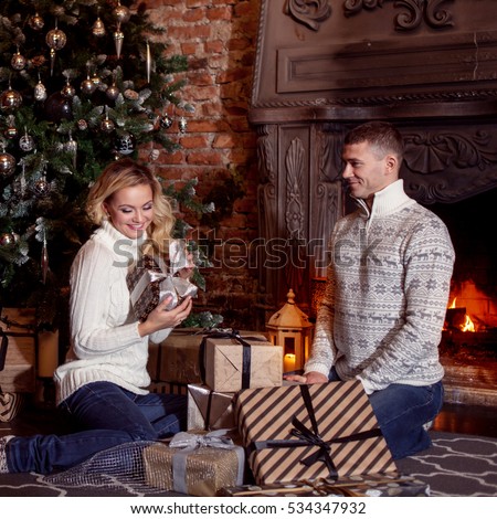 Young couple examines the gifts under Christmas tree. Holiday