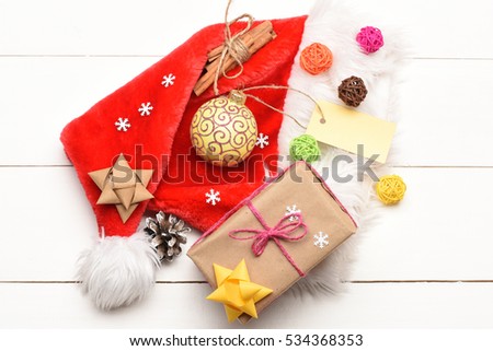 Colorful Christmas or New Year decoration of gift with rose string, yellow bow, yellow ball, Santa Claus red hat, brown bow, clews, pine cone, cinnamon, tag and snowflakes on vintage wooden background