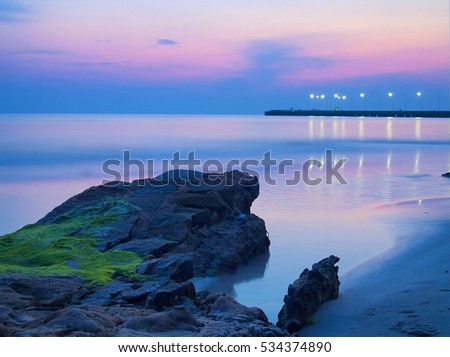 The blue hour image of wet rock with moss and sea weed on the ocean cliff with the jetty in backgroun during sunrise