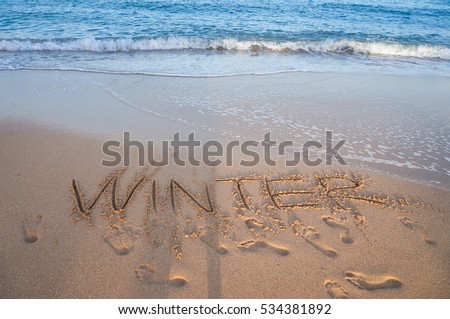 Winter word on a sandy beach with water slashes running on seashore. Seascape background with man shadow
