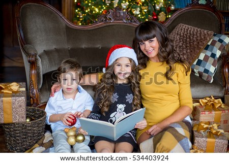 happy mother, little girl and boy reading a book over living room and christmas tree background