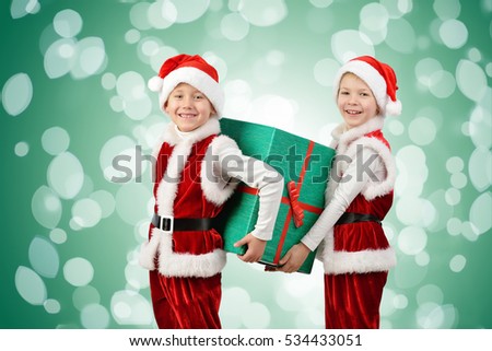 Adorable happy boys in santa clothes holding Christmas gift box. Isolated on green background with lights. Holidays, new year, x-mas concept.