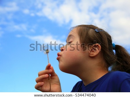 Little girl blowing dandelion on background of the blue sky Royalty-Free Stock Photo #534474040