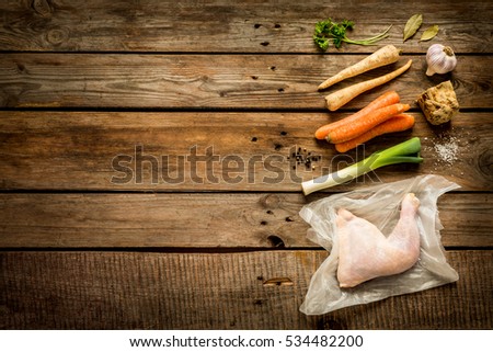 Cooking - chicken stock (bouillon, soup) recipe ingredients on rustic wooden background. Poultry and root vegetables - kitchen scenery from above (top view, flat lay). Layout with free text space.
