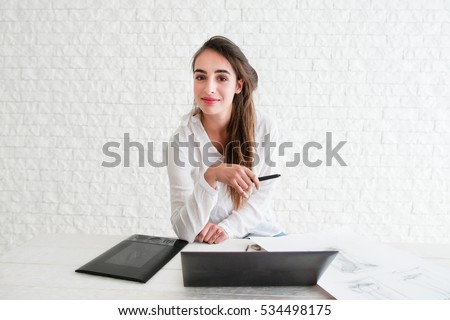 Female designer looking at camera on workplace. Beautiful confident woman sitting at desk with laptop and graphic tablet while working. Creativity, art, business, work concept