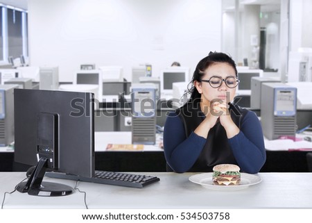 Picture  of obesity businesswoman with computer and hesitate to eat cheeseburger in the workplace