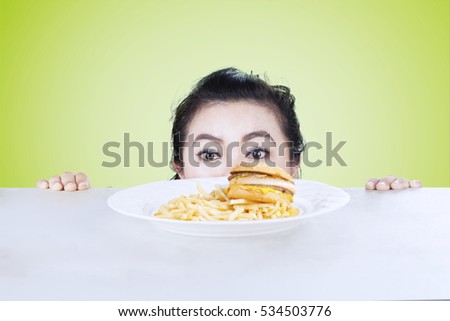 Picture of an adult woman is peeping hamburger on the table, shot with green background