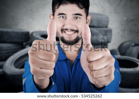 Close up of middle eastern mechanic showing two thumbs up and standing with stacks of old tires