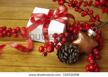 christmas present with wild rose fruits, cone and bauble on wooden background