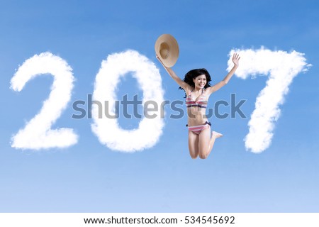 Concept of New Year 2017. Picture of of cheerful woman leaping on the sky with number 2017 and wearing swimsuit