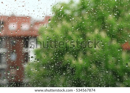 Rain drops on window with building and green tree in background