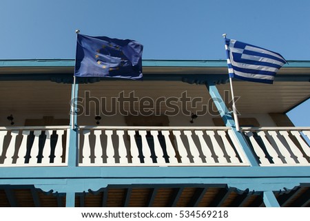 European Union flag and Greek flag on a pole on the balcony of wooden building, waving in the wind