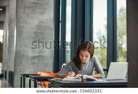 Shot of young asian female student sitting at table and writing on notebook. Young female student studying in library. Royalty-Free Stock Photo #534602335