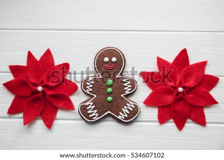Gingerbread man and felt flower Poinsettia laying on white wood background