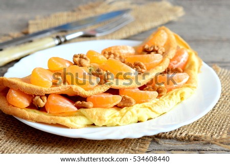 Fruit and nut omelette. Sweet fried omelette stuffed with fresh tangerines and walnuts on a plate. Knife, fork, burlap textile on an old table. Morning breakfast omelette. Healthy lifestyle. Closeup