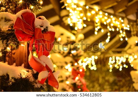 Snow covered red bow and evergreen garland spiraling posts with lights at night