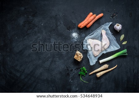 Cooking - chicken stock (bouillon, soup) recipe ingredients on black chalkboard background. Poultry and root vegetables - kitchen scenery from above (top view, flat lay). Layout with free text space.
