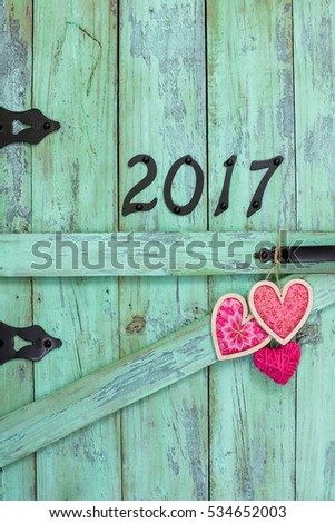 Year 2017 sign in black iron numbers and pink country fabric hearts on antique rustic mint green wood door; Valentines Day or Mothers Day background with painted wooden copy space for text