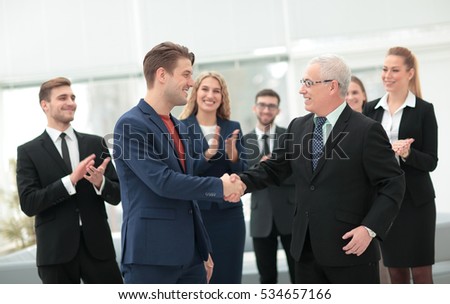 Two cheerful business people shaking hands while their colleague