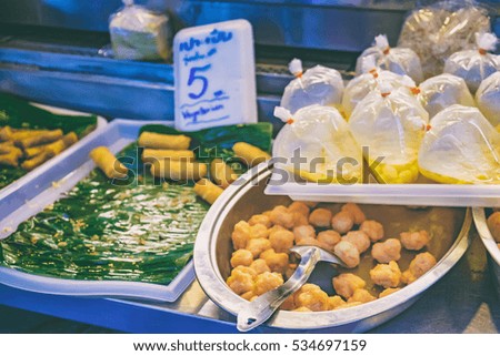 Spring Rolls on a banana leaf and Balls with price tag at Thai street night market. Deep fried snacks with different fillings and thai sauce in packets, fresh and hot food