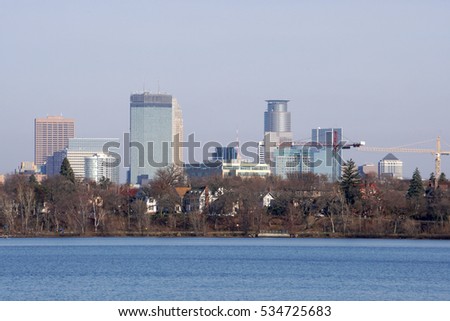 Minneapolis Minnesota skyline. Closeup skyscrapers tower over tree line and beautiful blue lake in winter. Buildings downtown financial district bank headquarters.