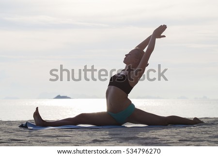 Happy young woman practicing yoga on the beach at sunset. Healthy active lifestyle concept