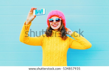 Fashion happy smiling woman taking picture self portrait on smartphone over blue background