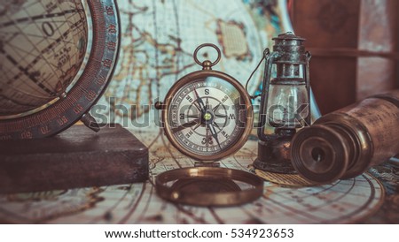 Antique pirate rare items collections including with a brass pocket compass with cover lid, retro oil lamp, telescope, globe model rotation on a wooden base on ancient world map. (vintage style)