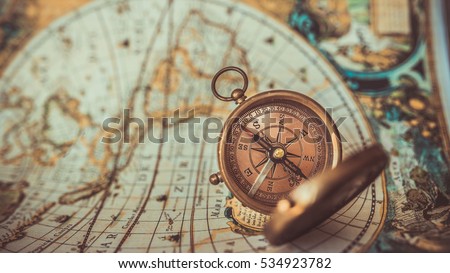 Old compass with cover lid on ancient world map background; a pirate rare item collection. (vintage style) Royalty-Free Stock Photo #534923782