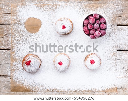 Fresh donuts (sufgania) with red jelly jam and fresh frozen cherries on a sugar powder and wooden background. Hanukkah holiday celebration and traditional jewish sweet