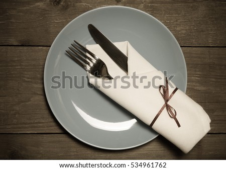 Plate, fork and knife in napkin on wooden background. Toned.