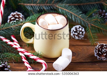 Close view at mug with hot chocolate, christmas tree, tangerines, peppermint stick and marshmallow on a wooden background. Dark photo.