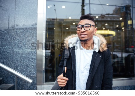 Image of a cheerful african young man walking on the street. Looking aside.