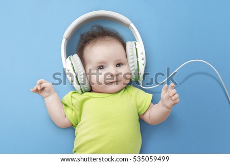 Pop music. Happy smiling newborn baby  listens to music in headphones on  blue background. Cheerful children's portrait