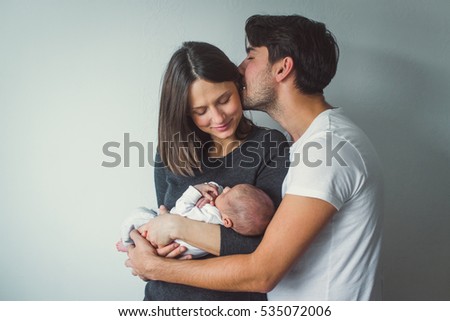 Woman and man holding a newborn.  A man kisses a woman. Royalty-Free Stock Photo #535072006